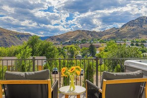 A balcony with outdoor furniture, a table with a vase of flowers, and a view of a town and mountains. - Hot Tub, Mt Views, Luxury New build in Golden (Golden)