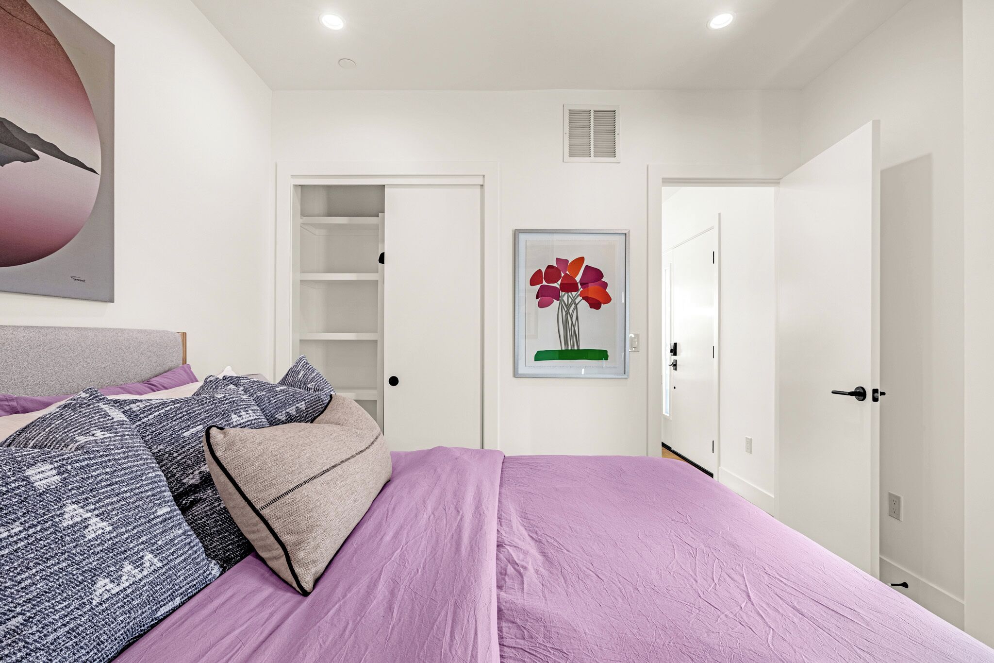 A bedroom with a bed, pillows, a wardrobe, a door, and a wall-mounted artwork.