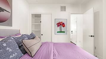 A bedroom with a bed, pillows, a wardrobe, a door, and a wall-mounted artwork.