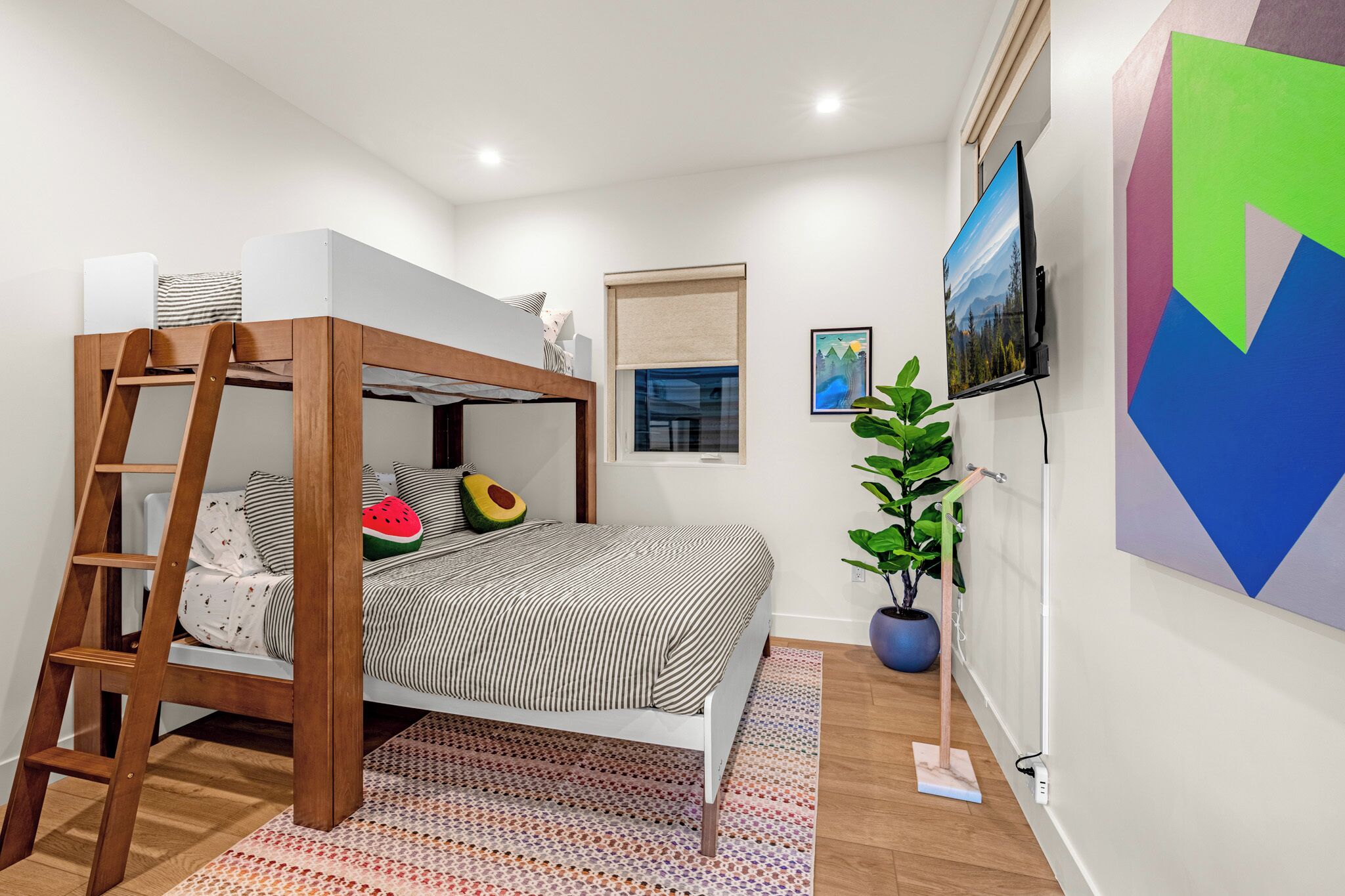 Une chambre avec un lit superposé, une échelle, une plante en pot, un téléviseur et des œuvres d’art accrochées au mur.