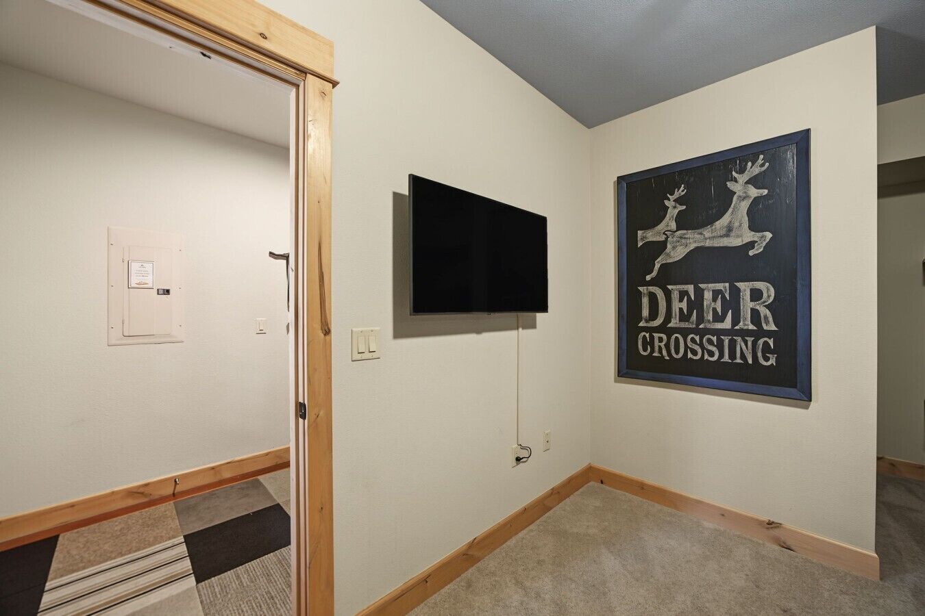 A hallway with a door, a mounted television, and a wall sign that reads 'DEER CROSSING'.