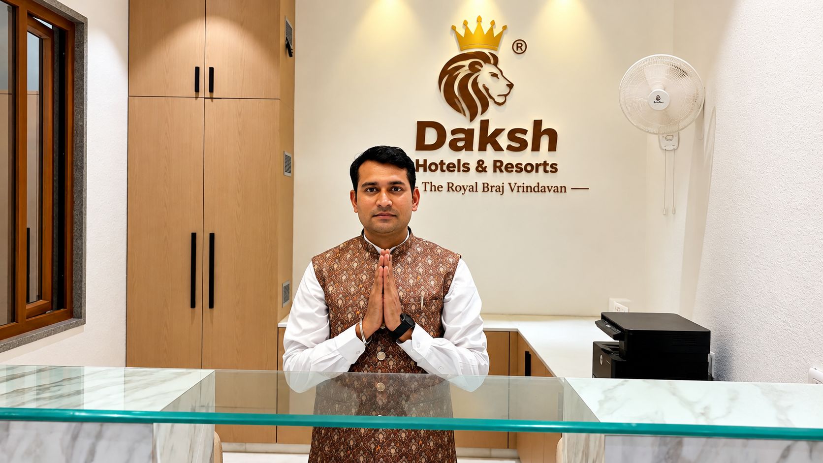 Zona de recepción de un hotel con mostrador de vidrio, armarios de madera y logotipo de Daksh Hotels & Resorts.