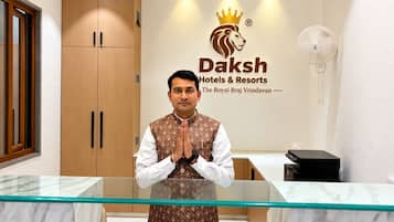 Zona de recepción de un hotel con mostrador de vidrio, armarios de madera y logotipo de Daksh Hotels & Resorts.