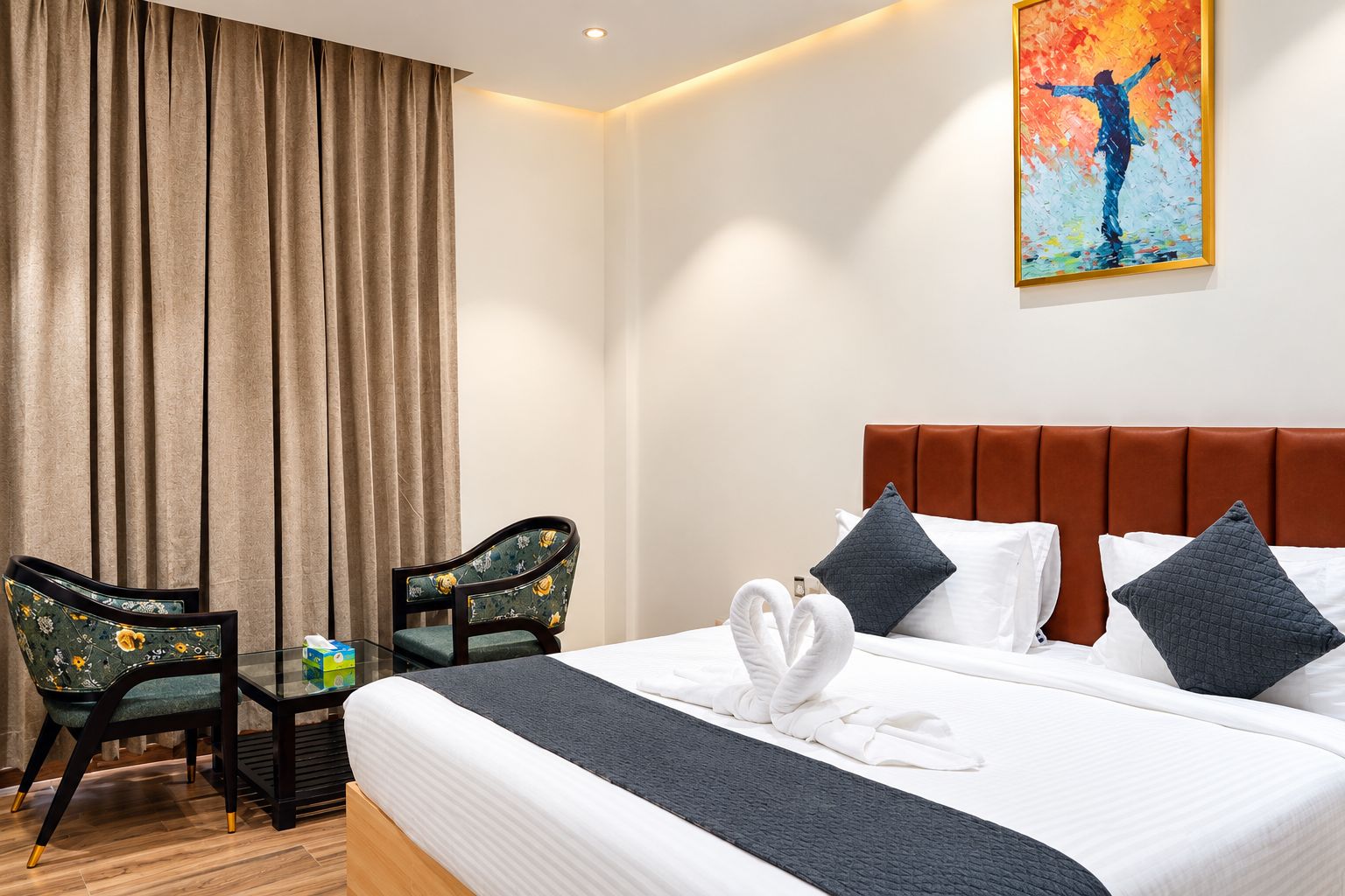 A hotel room with a bed, two chairs, a painting, and a curtain.