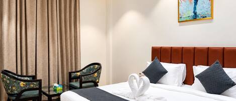A hotel room with a bed, two chairs, a painting, and a curtain.