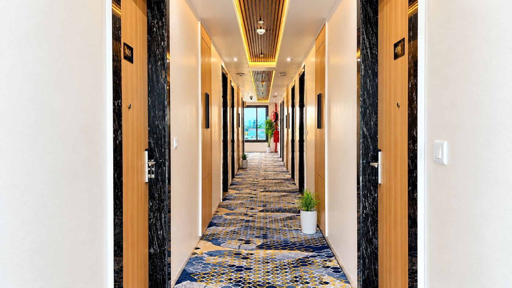 Un pasillo de hotel con alfombra estampada, puertas de madera y un diseño moderno en el techo.