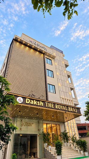 Un hotel con un letrero llamativo que dice 'Daksh The Royal Braj' y una fachada moderna con un diseño de pared con motivos.