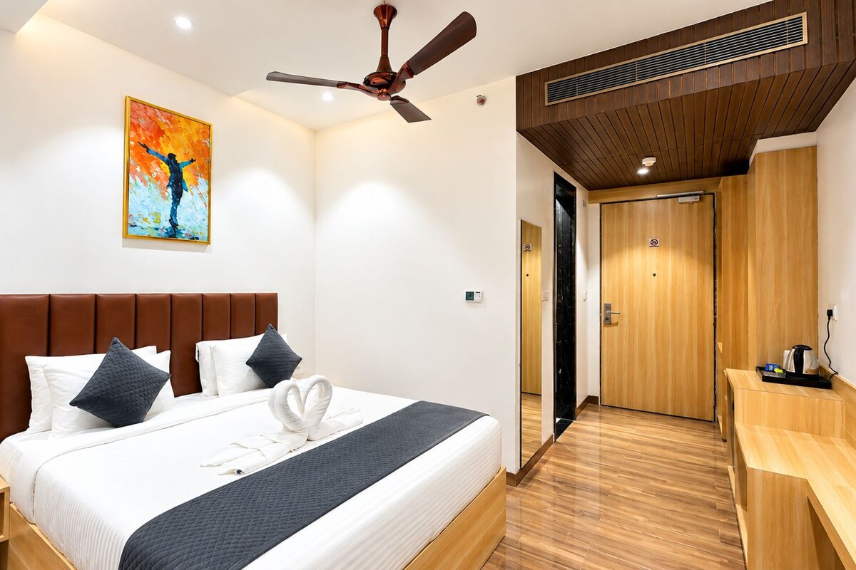A hotel room with a bed, a ceiling fan, a painting, and a wooden desk.
