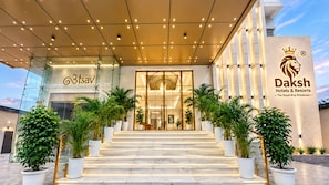 A hotel entrance with a glass facade, a staircase leading up to the entrance, and potted plants on either side. - Daksh The Royal Braj Vrindavan (Vrindavan)