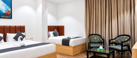 A hotel room with two beds, a ceiling fan, a painting, a window with curtains, and a small table with a chair.