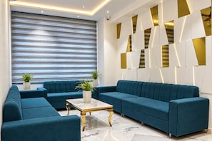 A modern living room with a sectional sofa, a coffee table, and two potted plants. - Daksh The Royal Braj Vrindavan (Vrindavan)