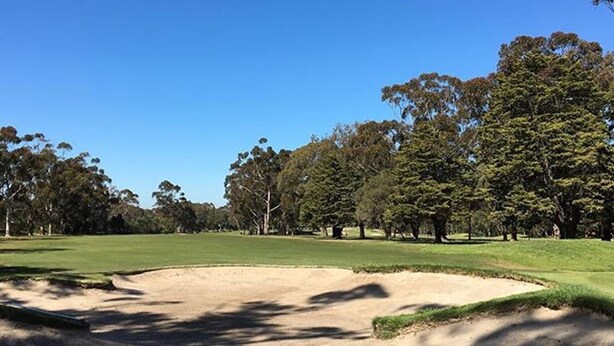 Ein Golfplatz mit einem Sandbunker, Bäumen und blauem Himmel.