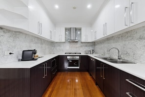 A modern kitchen with dark cabinetry, white countertops, a stainless steel sink, and a built-in oven. - Spacious 4-Bed House with Garden in Glenroy (Glenroy)