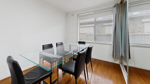 Ein Zimmer mit einem Glastisch, schwarzen Stühlen, einem Fenster mit Vorhängen und einem Holzboden.