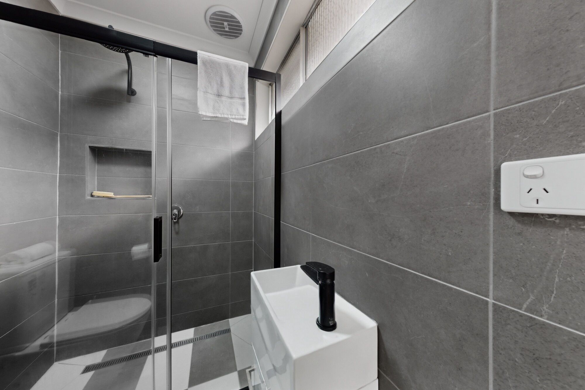 A modern bathroom with a glass shower enclosure, a white toilet, and a black faucet.
