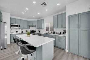 A modern kitchen with grey cabinets, a central island with bar stools, and built-in appliances. - 5B3B Sweet Home｜Near Strip｜Perfect for Families (Las Vegas)