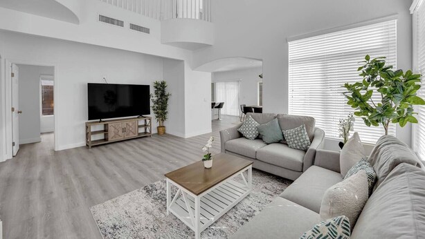 Uma sala de estar ampla com TV de tela plana, sofá, mesa de centro e escada para um andar superior.