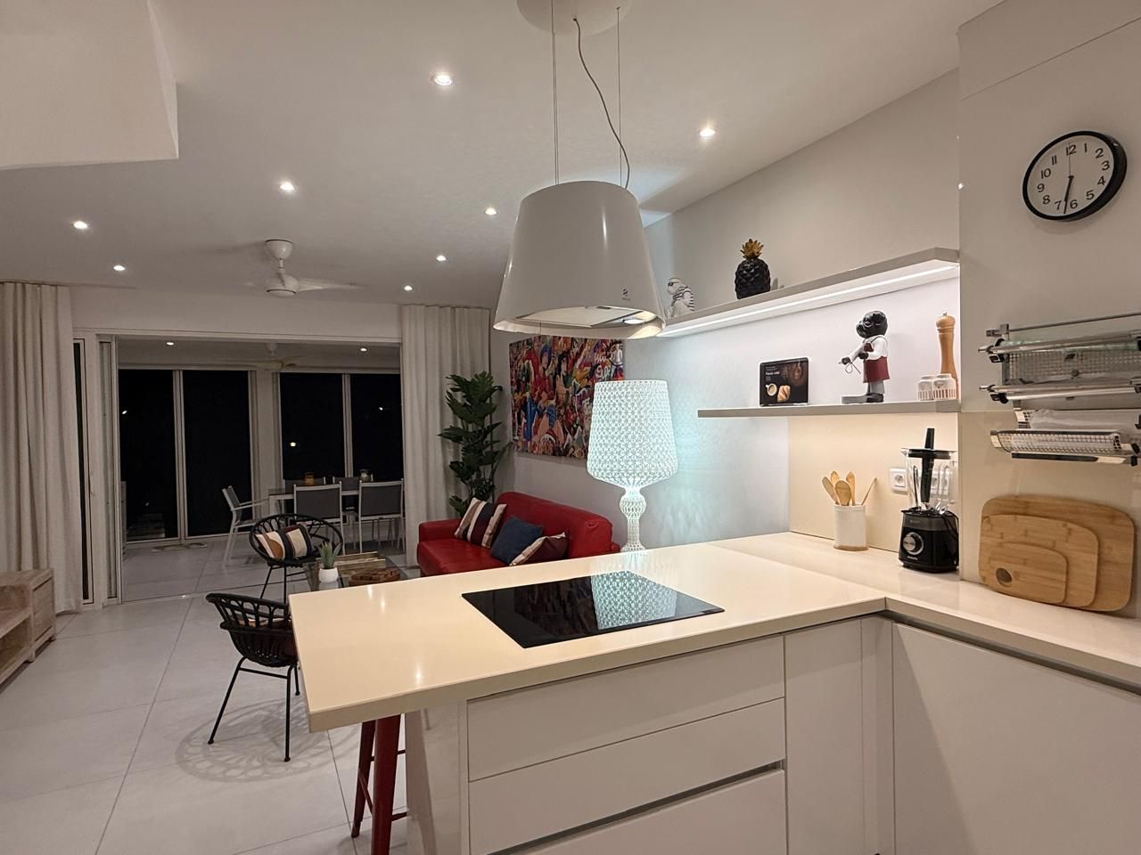 A modern kitchen with a central island, dining area with chairs, and a red sofa.