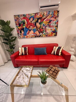 A red sofa with patterned cushions, a glass coffee table with a plant and a wooden tray, and a colorful superhero-themed artwork on the wall. - Luxury duplex in the heart of Baie Orientale, just a few steps from the beach (SAINT MARTIN)