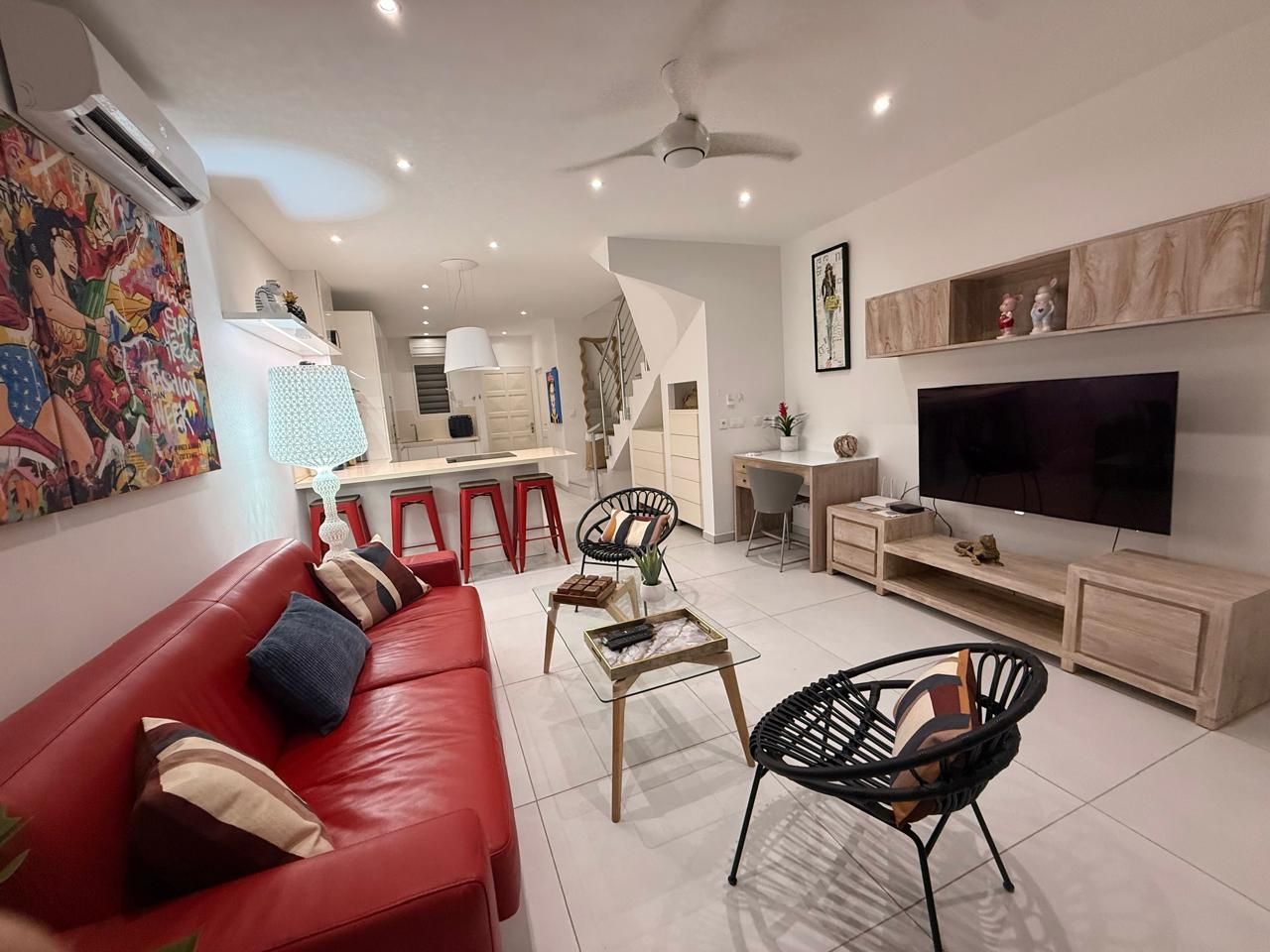 A modern living room with a red sofa, black chairs, a TV, and a kitchen area in the background.