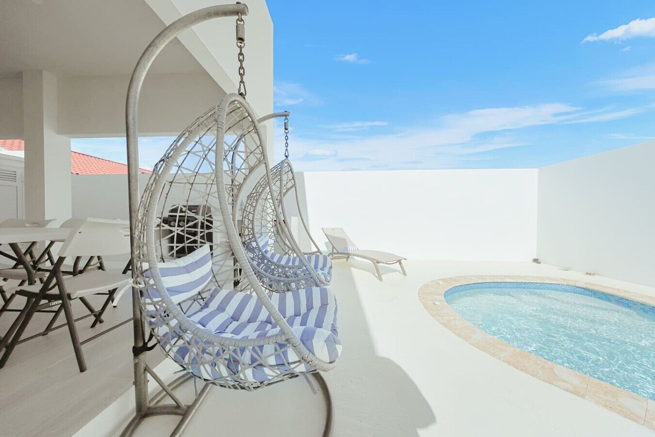 A poolside area with a hanging chair, lounge chairs, and a small pool.