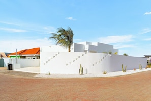 A modern building with a white facade, a palm tree, and cacti in a landscaped area. - 3BR Villa w/ Private Pool & Patio • Aruba Getaway (Noord)