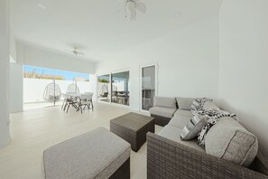 A modern living room with a sofa, a dining table, and chairs. There is a sliding glass door leading to an outdoor area. - 3BR Villa w/ Private Pool & Patio • Aruba Getaway (Noord)
