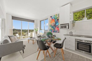 A modern kitchen with a dining area, large windows, and a view of the outdoors. - Breathtaking Luxury 2BR | 10 Min CBD | Water Views (Cammeray)