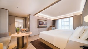 Quarto de hotel moderno com uma cama grande, uma escrivaninha, uma mesa redonda e uma televisão na parede.
