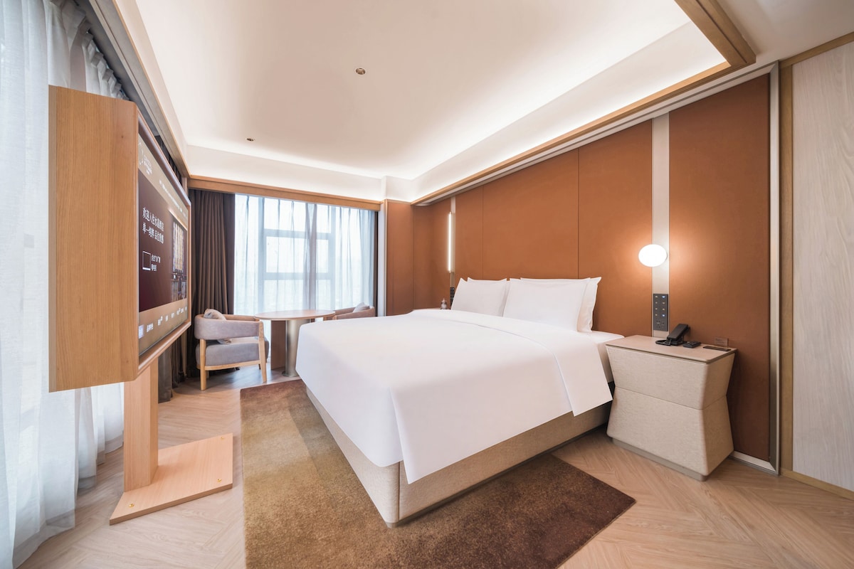 A hotel room with a large bed, bedside table, and a desk with a chair.