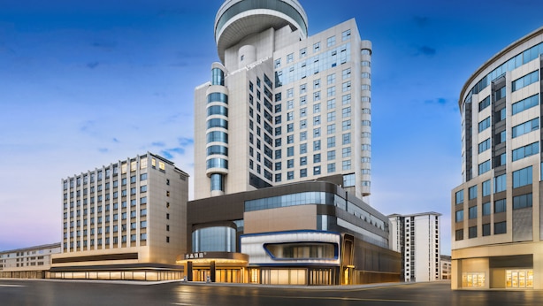 Um hotel moderno com fachada curva, vários andares e uma torre central imponente.