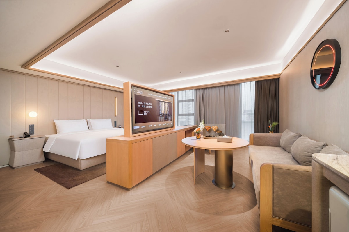 A hotel room with a bed, a desk, a round table, a sofa, and a TV.
