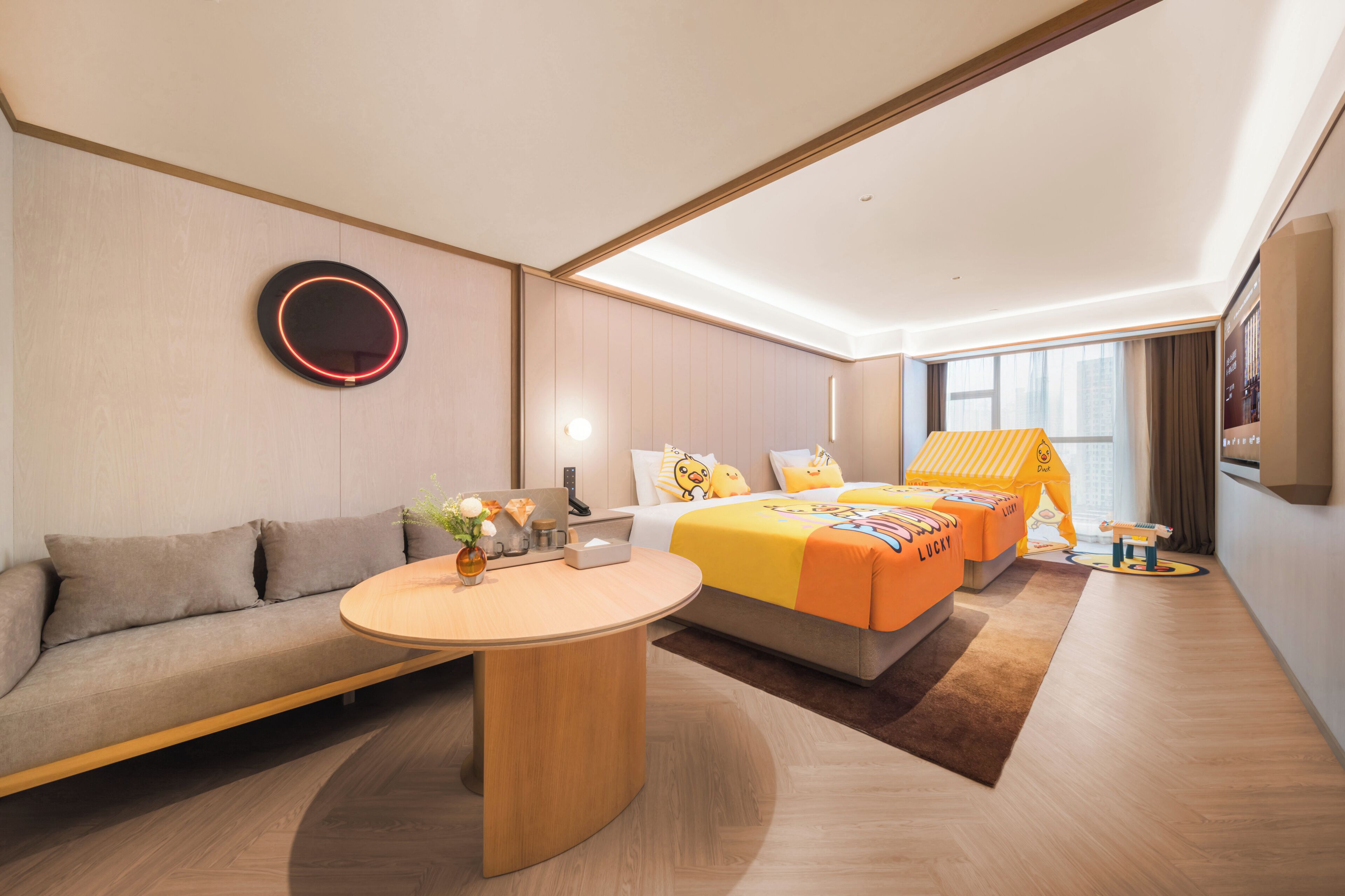 A modern hotel room with a sofa, a round table, a bed with a yellow canopy, and a large window.