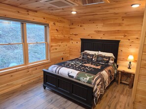 Una stanza con rivestimenti in legno, un letto, una finestra e un comodino con una lampada.