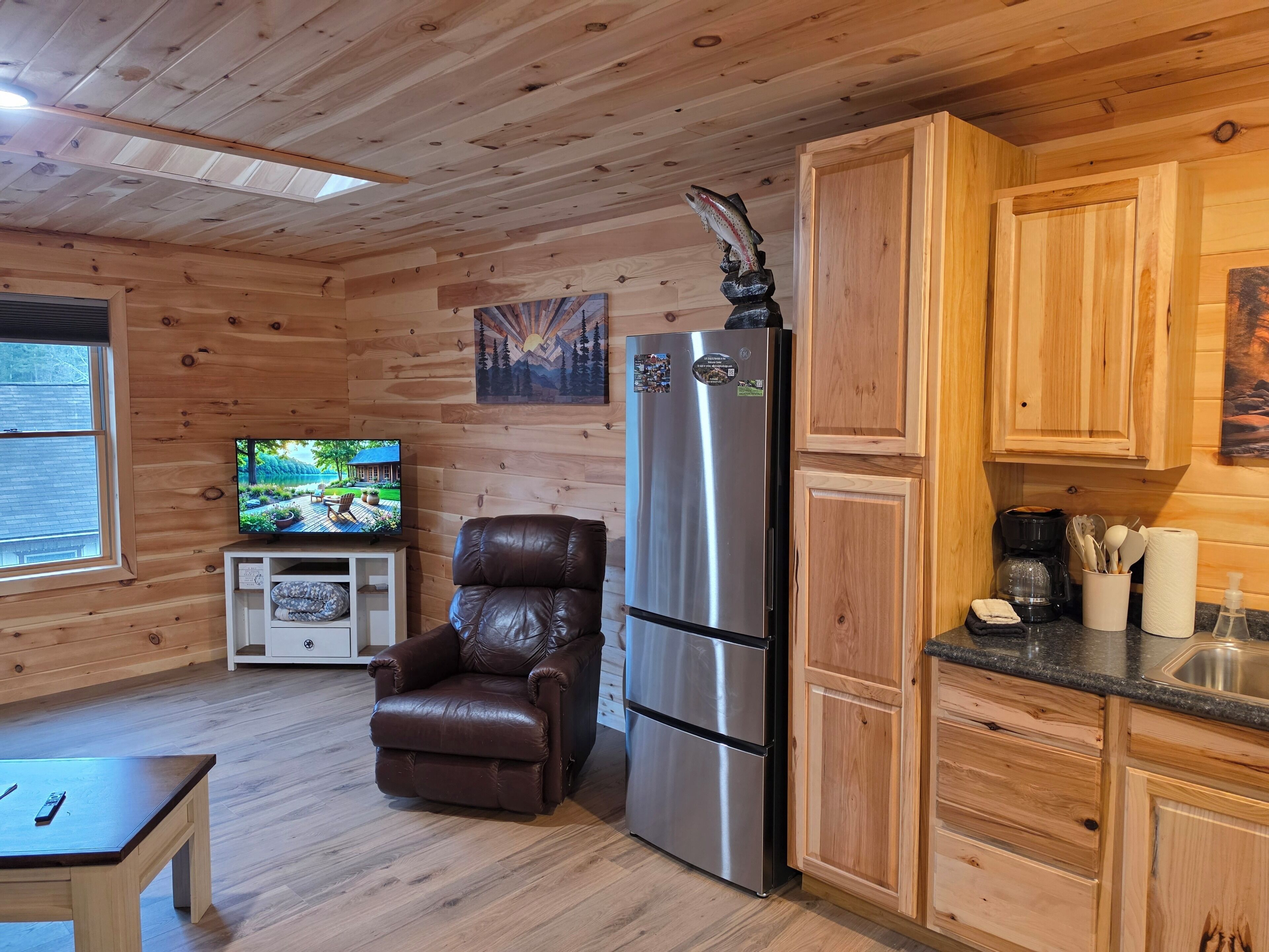 Un intérieur en bois avec un fauteuil en cuir, un réfrigérateur en acier inoxydable, un téléviseur et des armoires en bois.