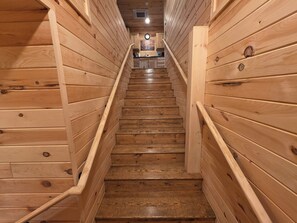 A wooden staircase with a handrail, leading to a room with a clock and a painting on the wall.