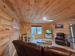 A cozy cabin interior with a wooden ceiling, a television, a refrigerator, and a leather sofa.