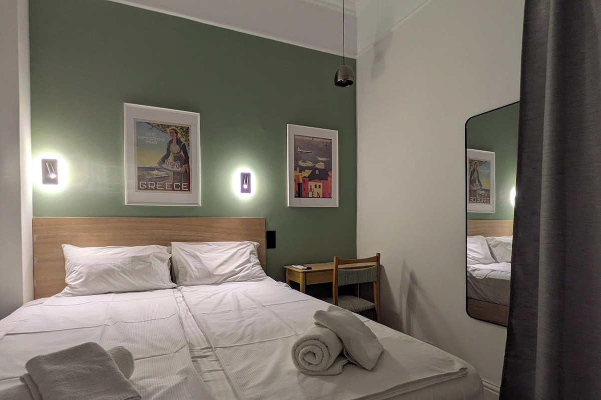 A hotel room with a bed, two wall-mounted lights, a desk, and two framed pictures.