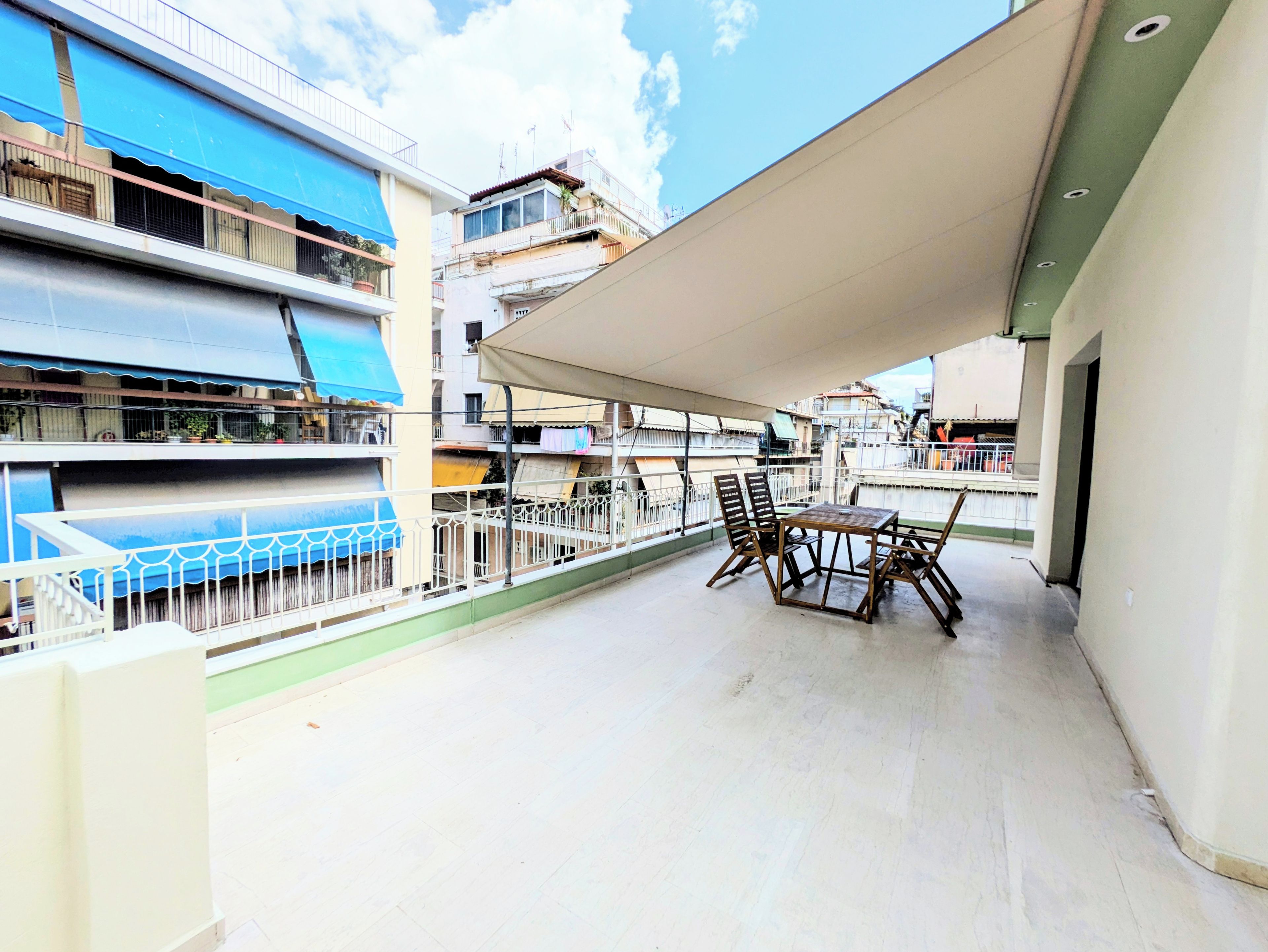 Uma varanda com mesa e cadeiras, um toldo azul e vista para edifícios vizinhos.