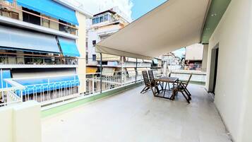 Uma varanda com mesa e cadeiras, um toldo azul e vista para edifícios vizinhos.