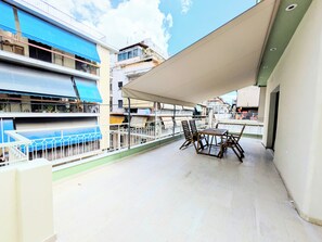 Uma varanda com mesa e cadeiras, um toldo azul e vista para edifícios vizinhos.