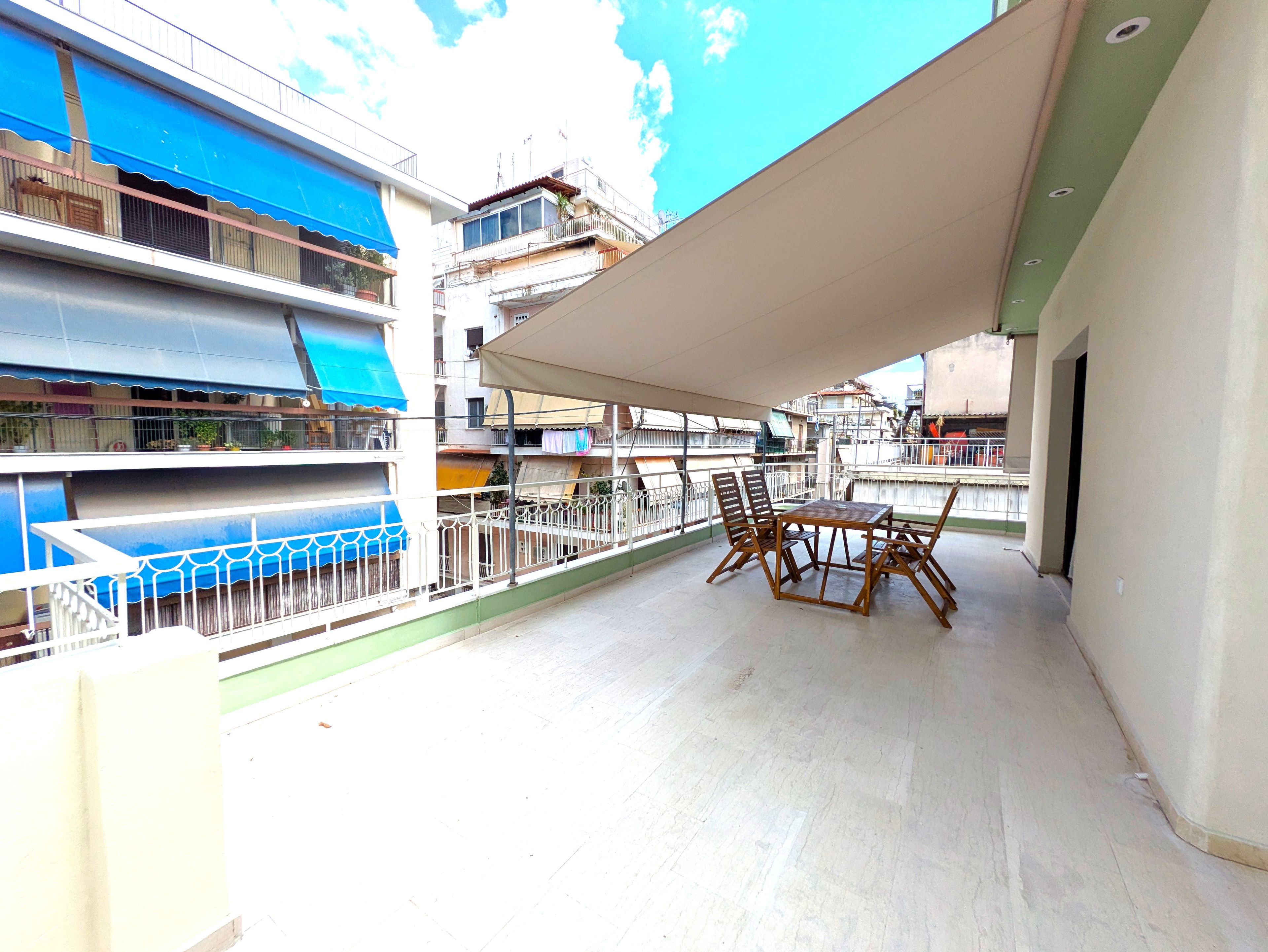 A balcony with a table and chairs, a blue awning, and a view of adjacent buildings.