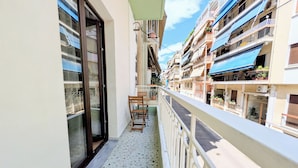 Un balcón con vistas a edificios cercanos, una puerta y una pequeña mesa con sillas.