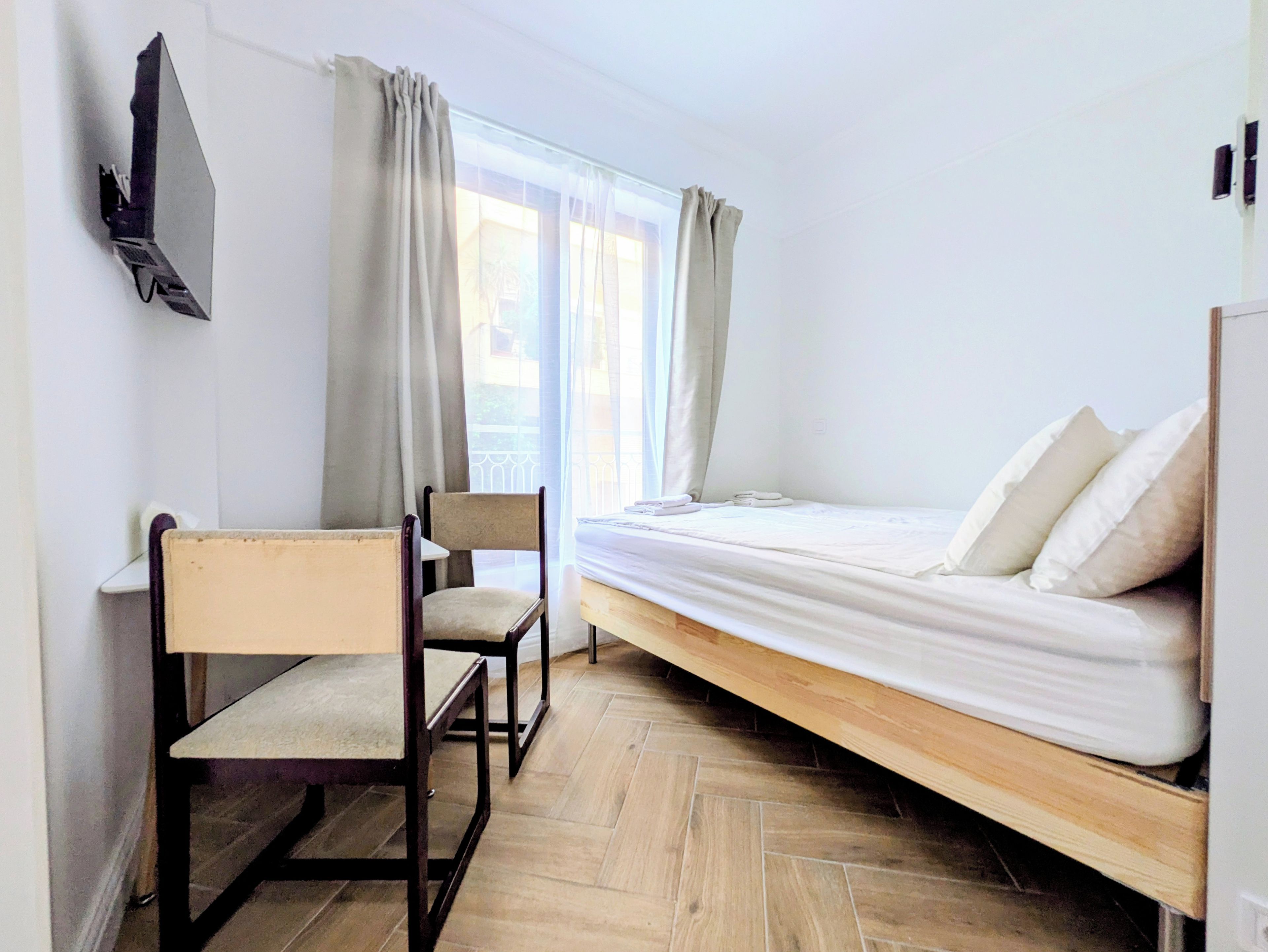 A room with a bed, a chair, a desk, and a TV mounted on the wall.