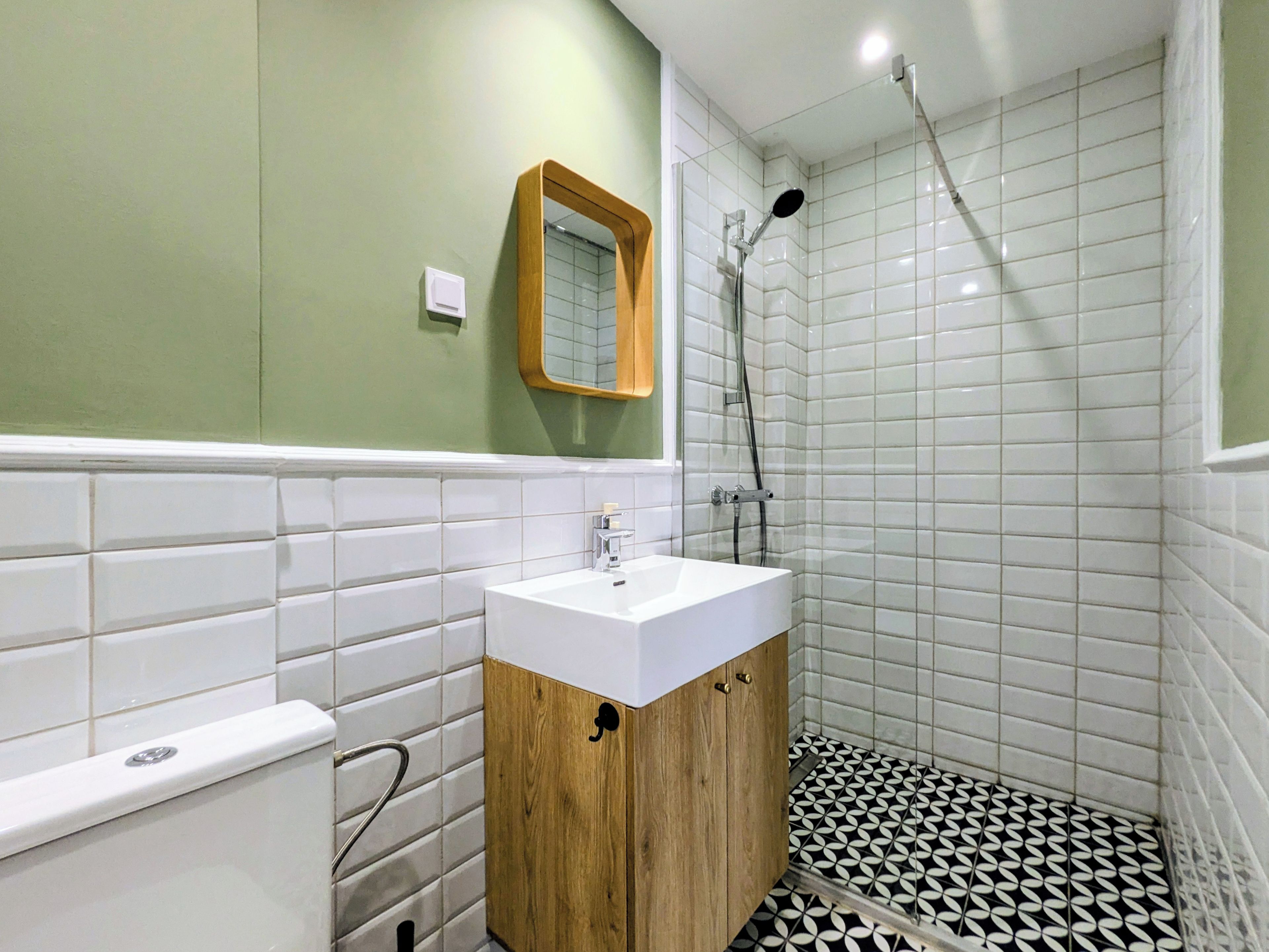 Un baño con lavamanos blanco, mueble de madera y zona de ducha con azulejos blancos.