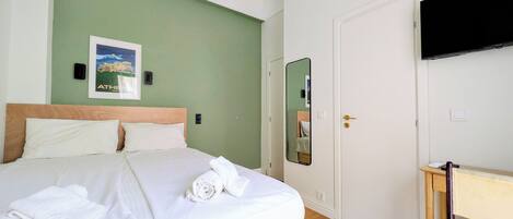 Een hotelkamer met een bed, een bureau, een stoel, een flatscreen-tv, een airconditioner, een deur en een spiegel aan de muur.