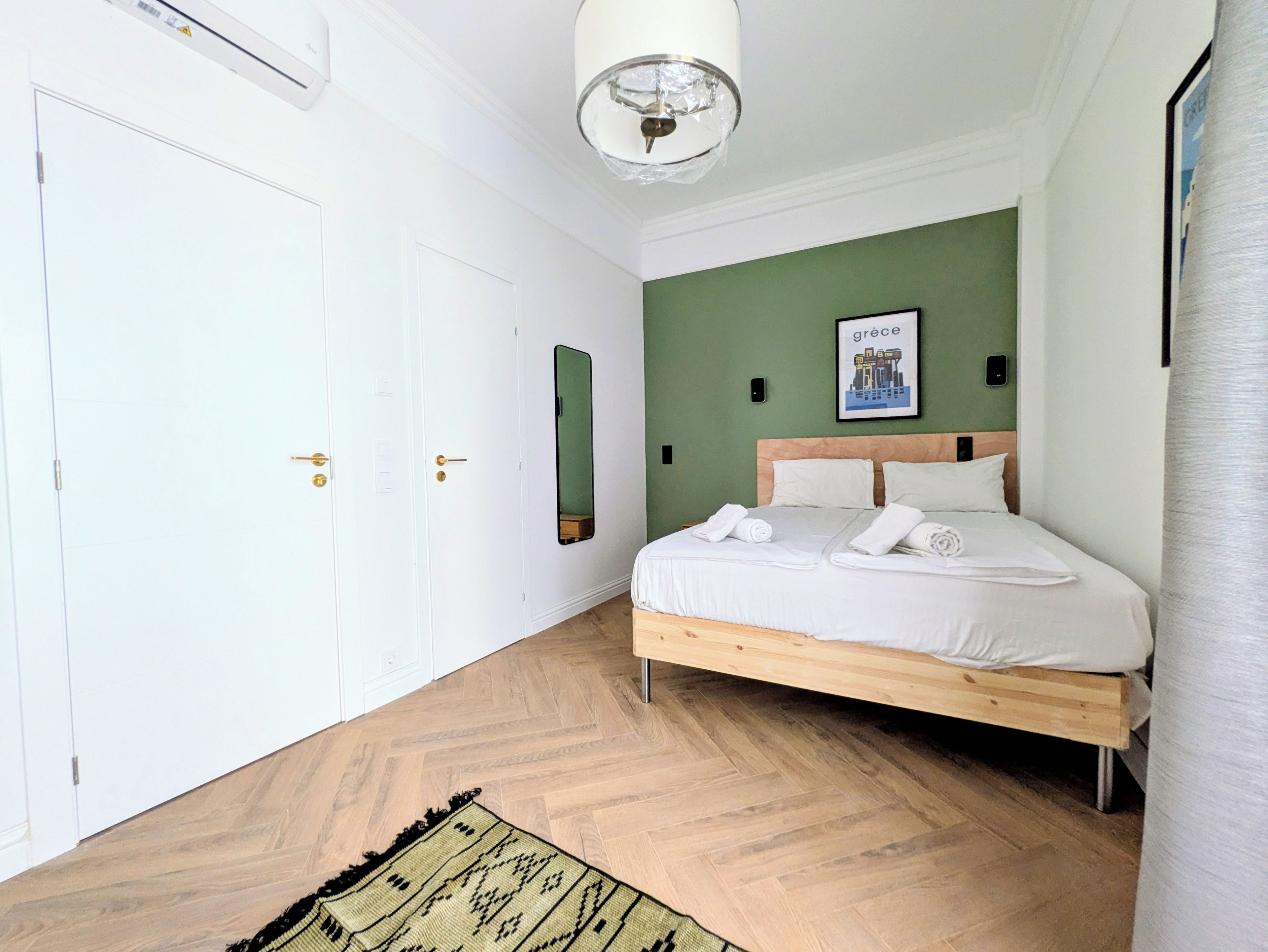 A bedroom with a bed, a door, a mirror, and a wall-mounted light fixture.