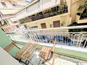 A balcony with a wooden table and chairs, overlooking a street with parked cars and a building with balconies. - Dinostratus House - Boutique Rooms and Apartments near Acropolis and Metro (Athina)