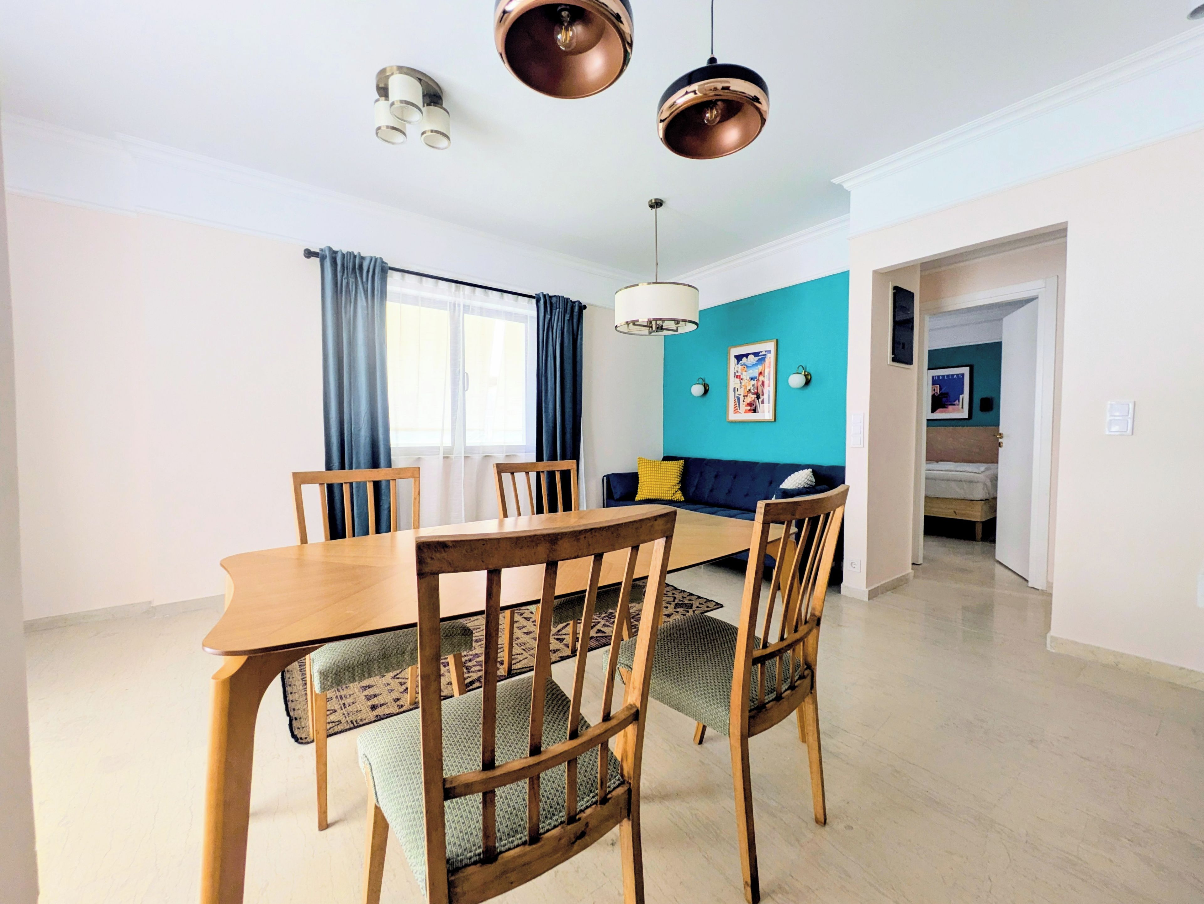 Een eetruimte met een houten tafel en stoelen, een bank en een blauwe accentmuur.