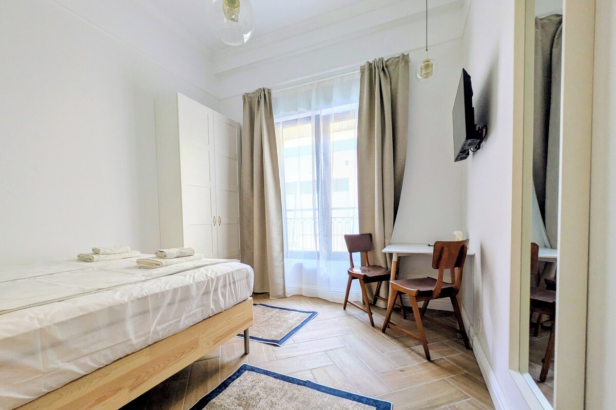 Ein Schlafzimmer mit einem Bett, einem Schreibtisch, einem Stuhl und einem Fenster mit Vorhängen.